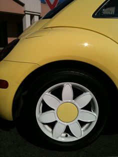 a yellow car with white spokes parked in a parking lot next to a building