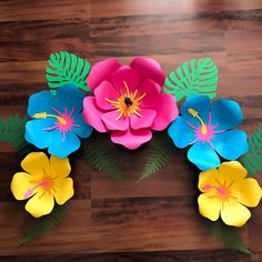 colorful paper flowers are arranged on a wooden surface with green leaves and palm fronds