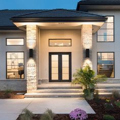 the front entrance of a modern home at night with lights on and flowers in the foreground