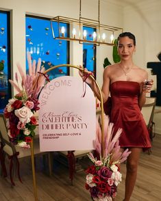 a woman in a red dress standing next to a sign with flowers and candles on it