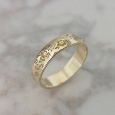 a gold wedding ring with flowers on the side and leaves in the middle, sitting on a marble surface