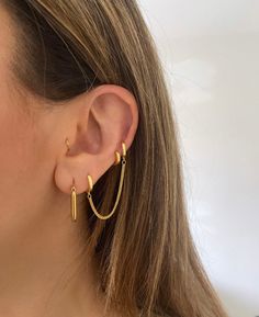 a woman wearing gold hoop earrings with small bars hanging from the end of each ear