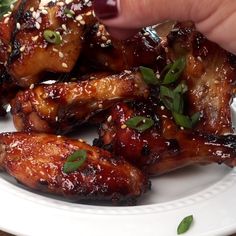 someone is dipping sauce on chicken wings with sesame seeds and garnished with parsley