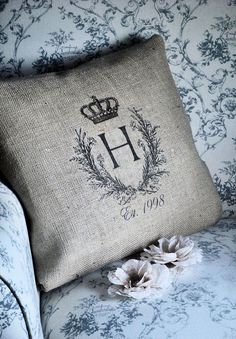 a pillow with the letter h on it sitting on a couch next to a flower