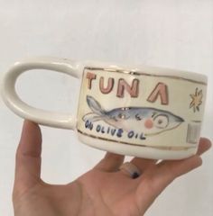 a hand holding a coffee mug with an image of a fish on the bottom and words that read, tuna in olive oil