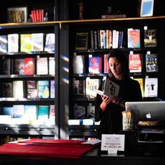 a woman standing in front of a bookshelf holding a book and looking at it