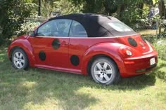 a red car with black polka dots on it's hood parked in the grass