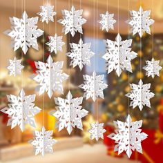 paper snowflakes hanging from strings in front of a christmas tree with presents on it