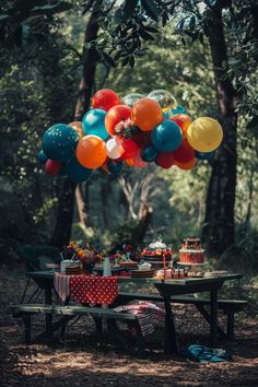 a picnic table with balloons and cake on it in the middle of a wooded area