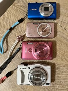 three different cameras sitting on top of a wooden table