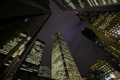 looking up at skyscrapers in the city at night with lights on and dark sky