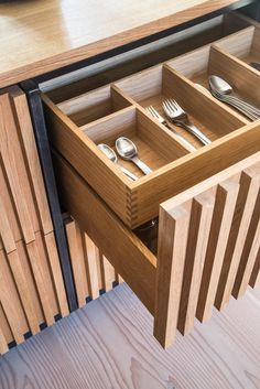 an open drawer with utensils and spoons in it on a wooden table