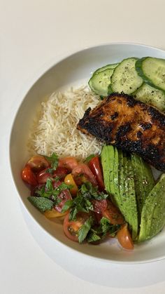 a white plate topped with rice, cucumber slices and other foods on top of it