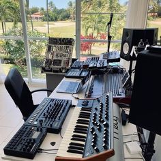 there are many electronic keyboards on the table in front of the window, and one keyboard is black