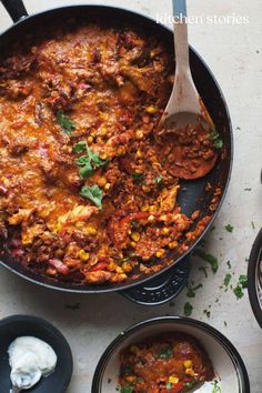 a skillet filled with mexican food next to two bowls of dip and sour cream