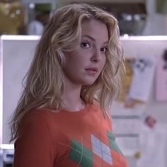 a woman in an orange shirt looking at the camera while standing next to a refrigerator