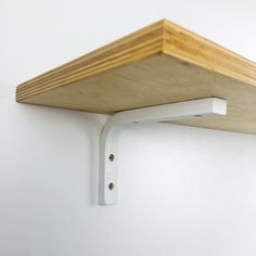 a wooden shelf mounted to the side of a wall next to a metal hook on a white wall