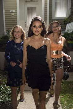 three women are walking down the sidewalk in front of a house, one is wearing a black dress