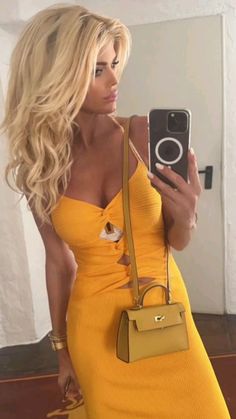 a woman in a yellow dress taking a selfie with her cell phone and purse