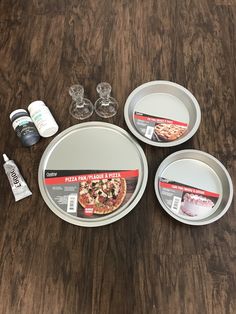 three pizza pans sitting on top of a wooden table next to empty wine glasses