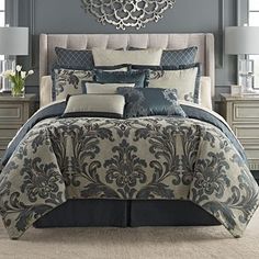 a bed with blue and grey comforters in a bedroom next to a mirror on the wall