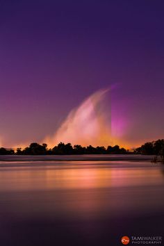 the sun is shining brightly in the purple sky above trees and water at night time