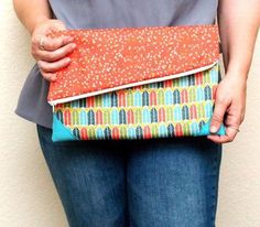 a woman holding an orange and blue purse with polka dots on the bottom, in front of a white wall