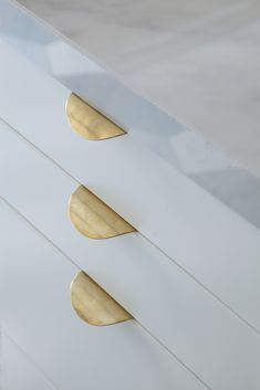 three white drawers with gold handles on each drawer and one has two oval knobs