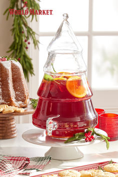 there is a red drink in the glass on the table with cookies and oranges