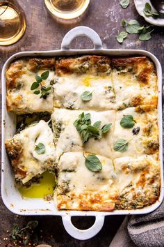 a casserole dish with cheese and spinach on top, surrounded by wine glasses