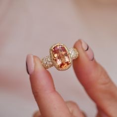 a close up of a person holding a ring with an orange and white stone in it