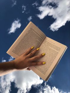 a woman's hand holding an open book in front of a blue sky with clouds