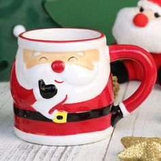 two santa claus mugs sitting next to each other on a white wooden table with gold stars