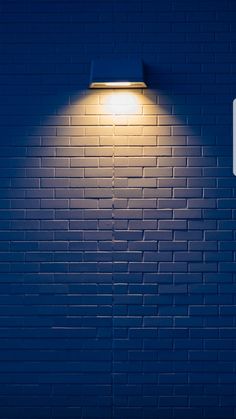 a blue brick wall with a lamp on it's side in the night time