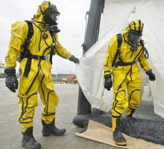 two men in yellow suits standing next to each other near a white sheet covered structure