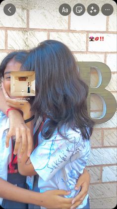 a man and woman hugging each other in front of a brick wall with the letters b on it