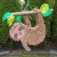 a paper mache sloth hanging from a branch with leaves on it's back