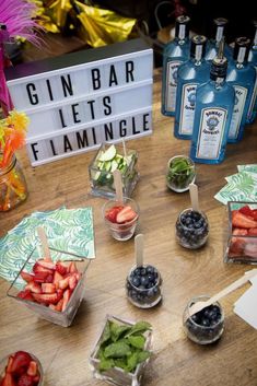 a wooden table topped with lots of fruit and veggies next to bottles of gin