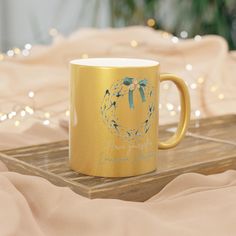 a gold coffee mug with a blue bow on it sitting on a wooden tray in front of some lights