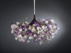 a chandelier with purple and white flowers hanging from it's side on a gray background