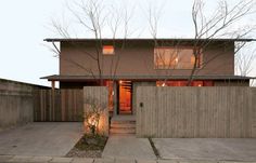 a house with a fence in front of it and trees on the sidewalk next to it