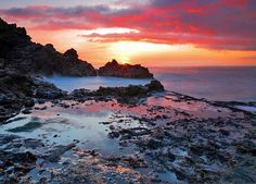 the sun is setting over some rocks and water