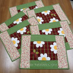 four quilted placemats with white flowers on red and green plaid fabric, sitting on a wooden table