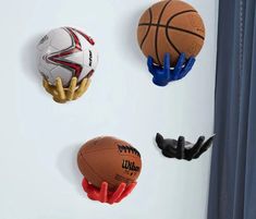 three sports balls are hanging on the wall next to gloves and basketballs in different colors