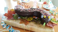 a birthday cake with chocolate frosting and leaves on a cutting board in front of a table