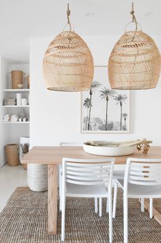 two wicker lamps hanging over a dining room table with white chairs and rattan placemats