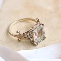 an engagement ring with a large green stone surrounded by small diamonds on top of a white cloth