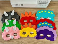 five masks are lined up on a table next to a sewing machine and thread spools