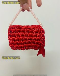 a hand holding a red purse with pearls on it's string and beaded handle