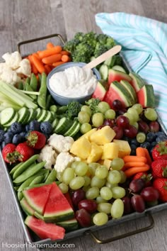 a platter filled with fruits and vegetables on top of a wooden table next to a blue towel